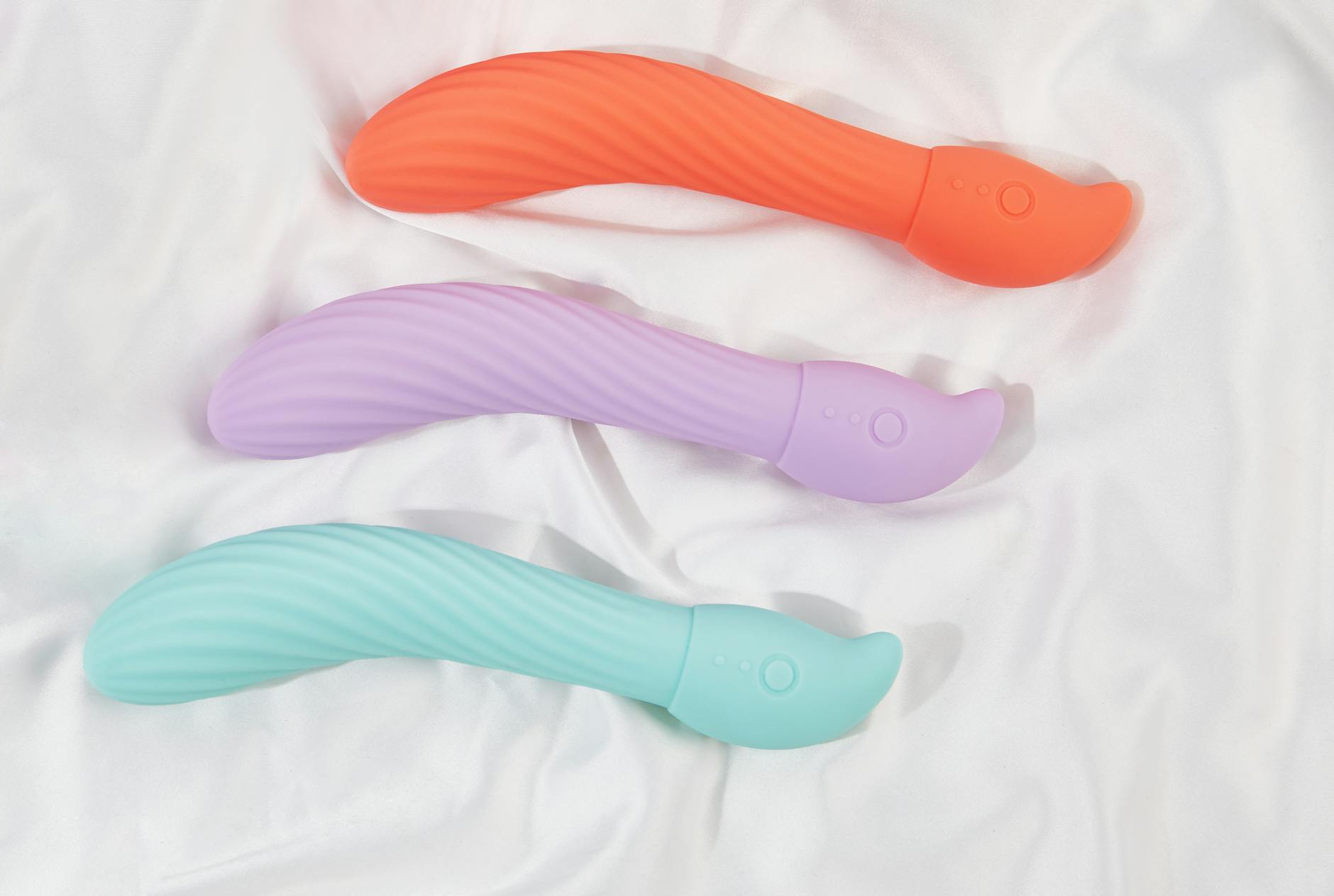 Three colorful vibrators arranged on white fabric highlighting their smooth design