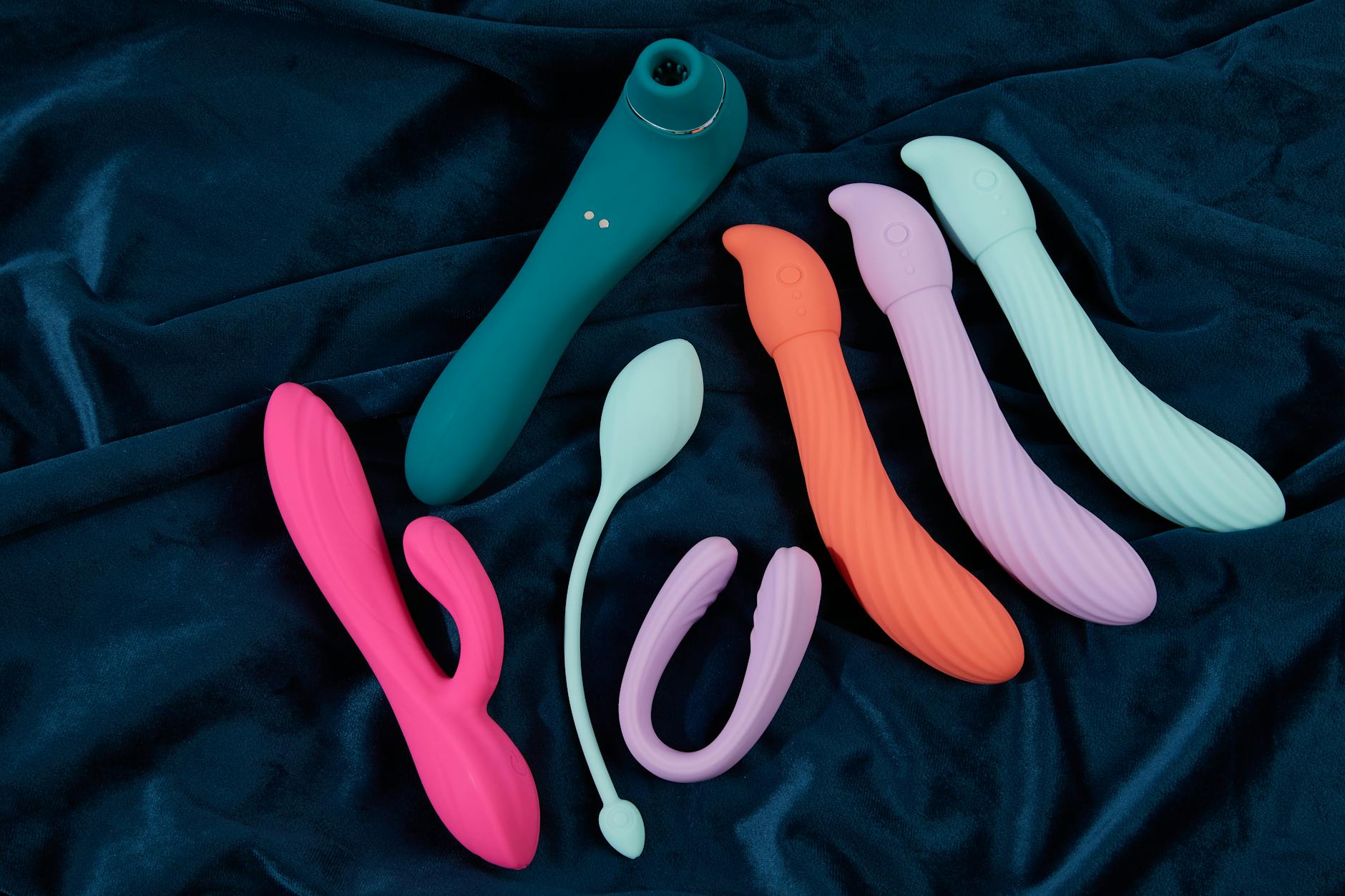 Vibradores de silicone em cores vibrantes dispostos em tecido azul escuro