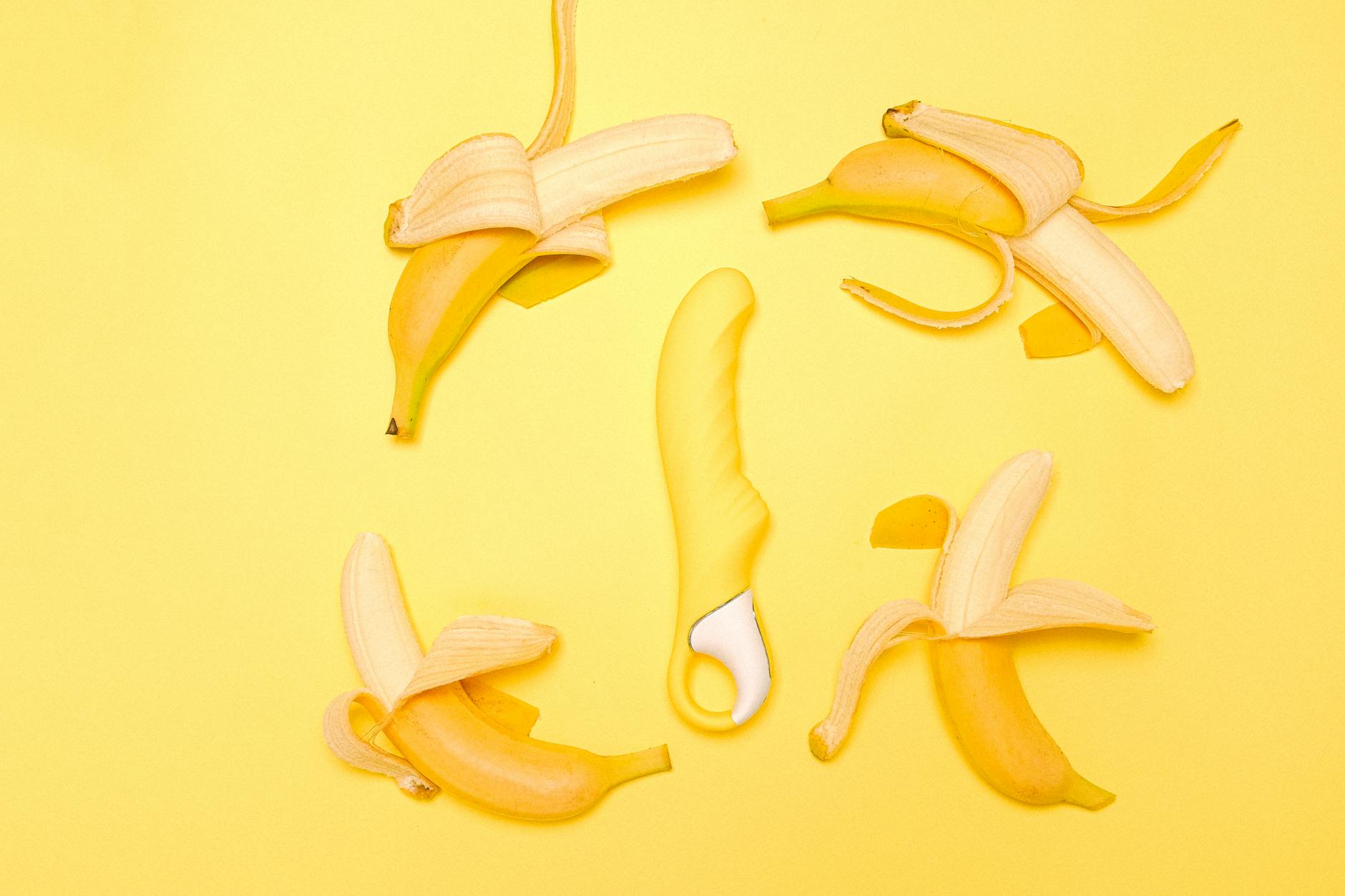 Yellow lemon clitoral vibrator surrounded by fresh peeled bananas on a bright yellow background
