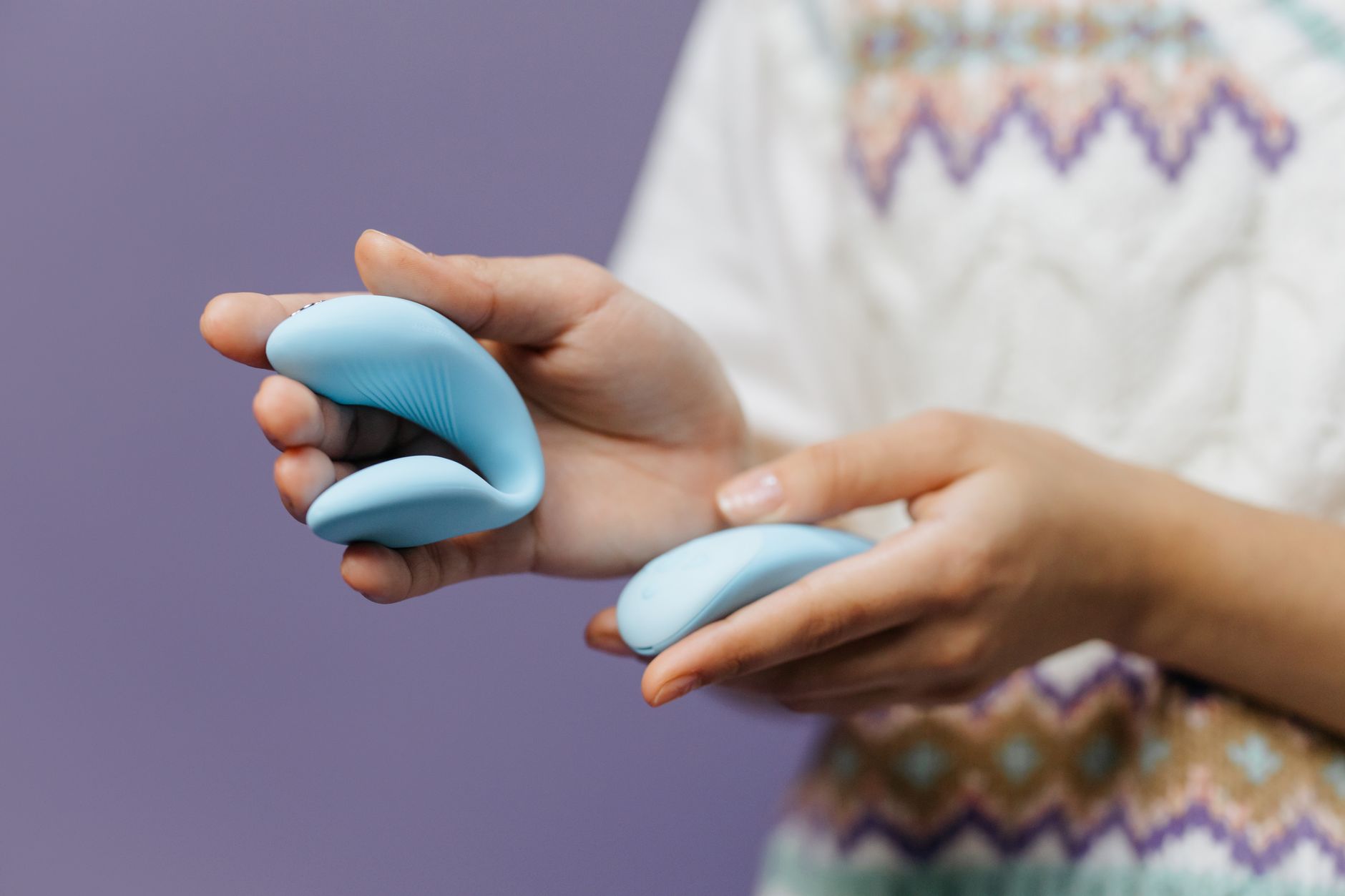 Close-up of hands holding a sleek blue vibrator, representing sensitive pleasure exploration.
