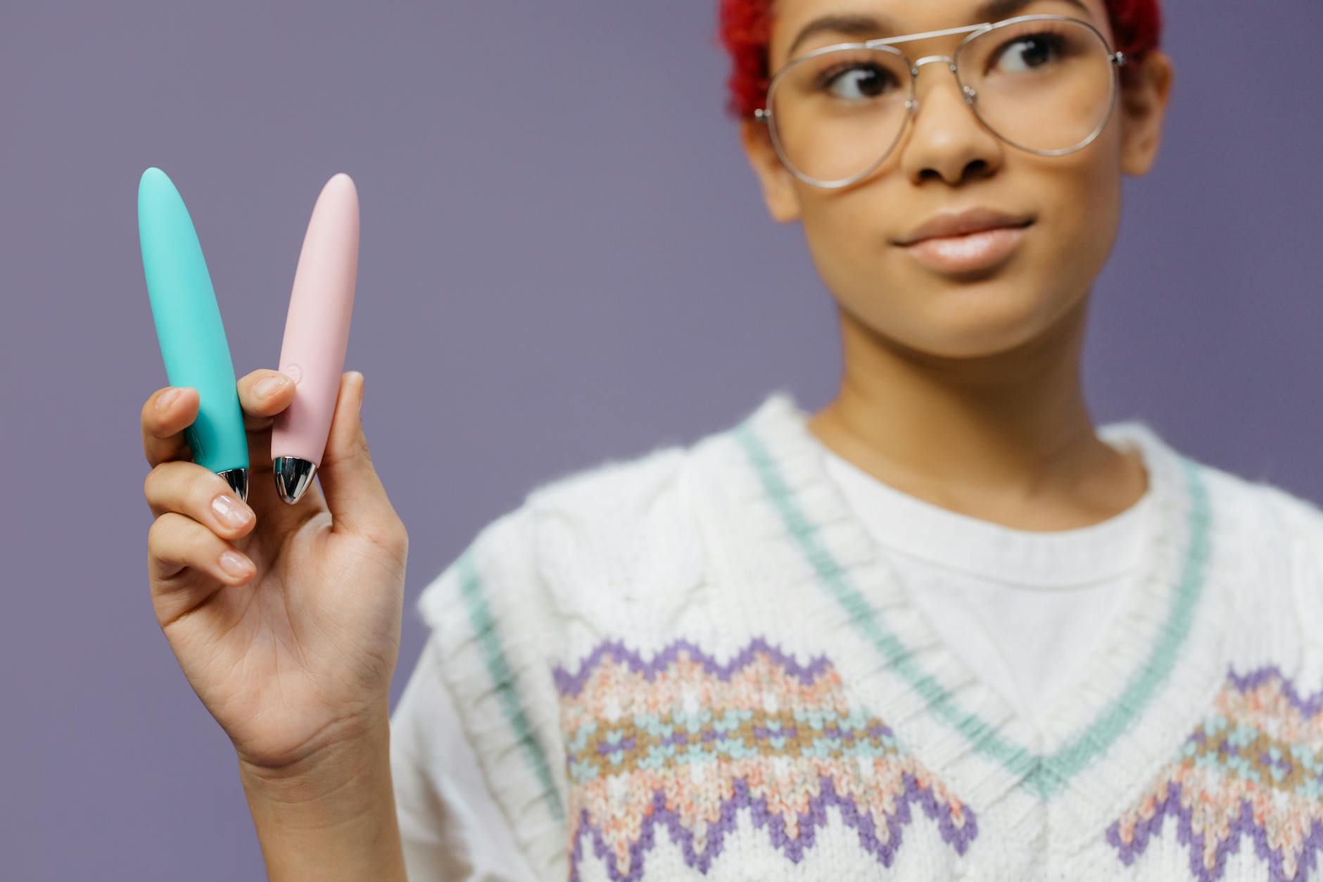 Woman holding colorful vibrators against a purple background, representing pleasure and control