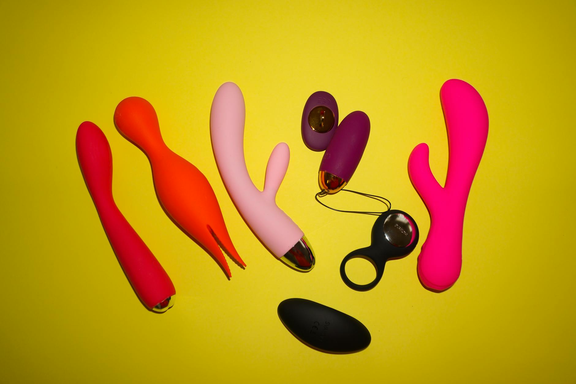 A yellow silicone vibrator surrounded by fresh fruits on a bright yellow background.