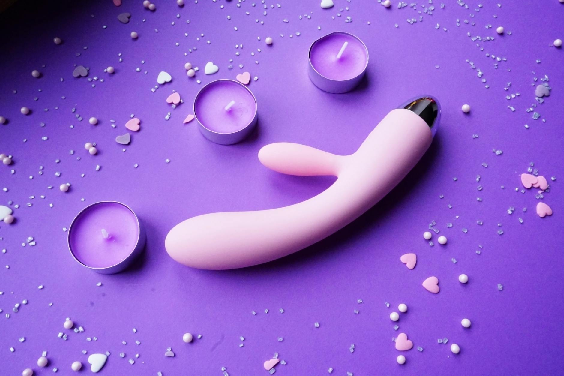 Vibrador rosa em fundo roxo com confete de coração e velas para clima romântico